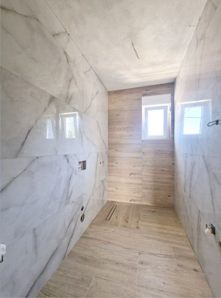 A bathroom in a 3-room apartment with marble tiles and a wooden decor floor.