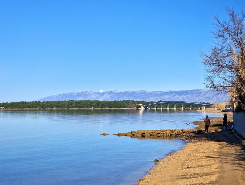 The coast in Privlaka with a view of the bridge and mountains in the background.