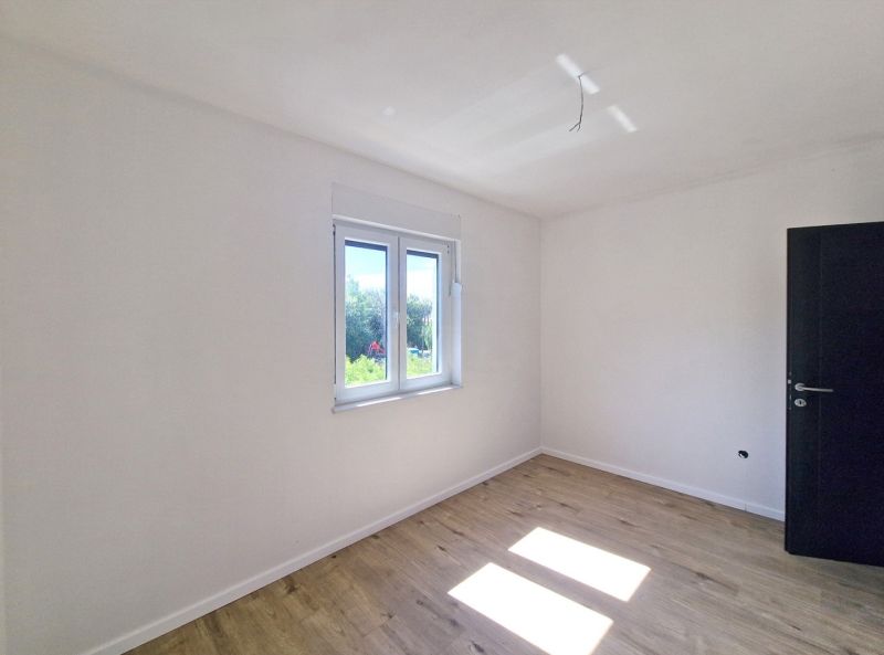 A white room in a 3-room apartment with a wood-patterned floor and a window.