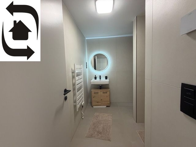 A bathroom in a 2-room apartment with a round mirror and a wooden cabinet under the sink.