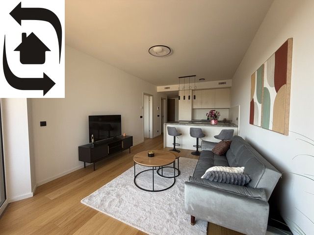 Living room of a two-room apartment with a wooden decor floor, a sofa, and a television.