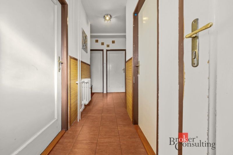 A corridor with white walls and doors in a 3-room apartment, brown tiles.