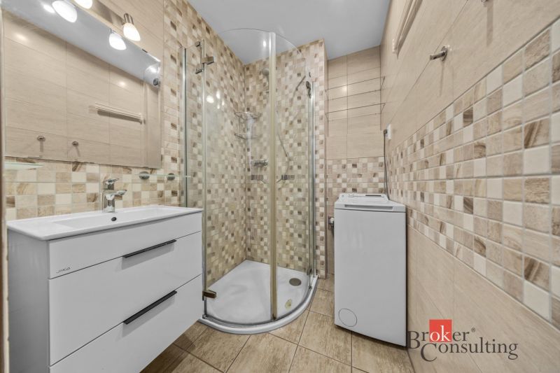 A bathroom in a 3-room apartment with mosaic tiles, a shower corner, and a washing machine.