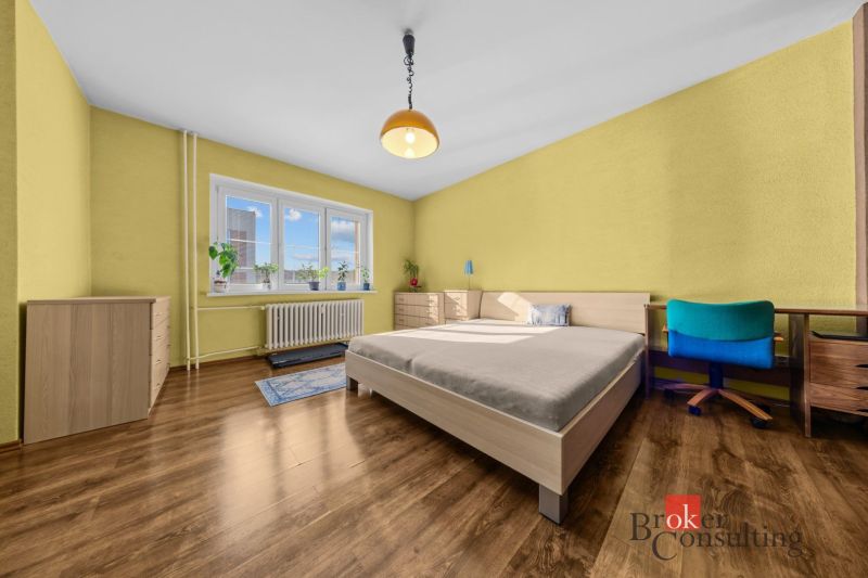 A kitchen in a 3-room apartment with a refrigerator, dining table, and wooden decor flooring.