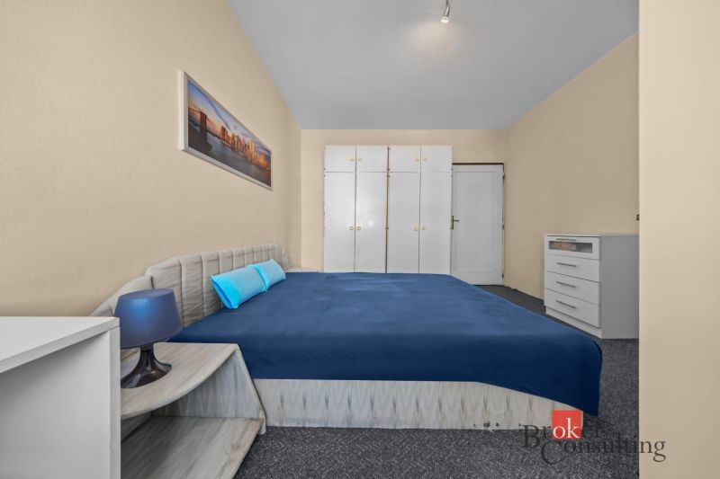 A bedroom in a 3-room apartment with a blue bed, white wardrobes, and a carpet.
