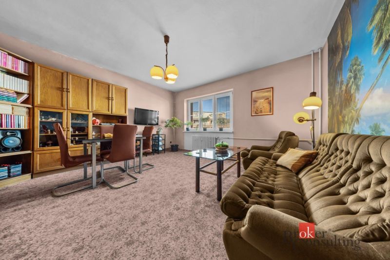 Living room in a 3-room apartment, with carpeted floor, bookshelf, and retro furniture.