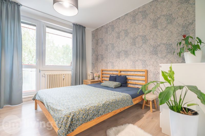 A bedroom with a double bed, a wooden decor floor, and plants in a 3-room apartment.