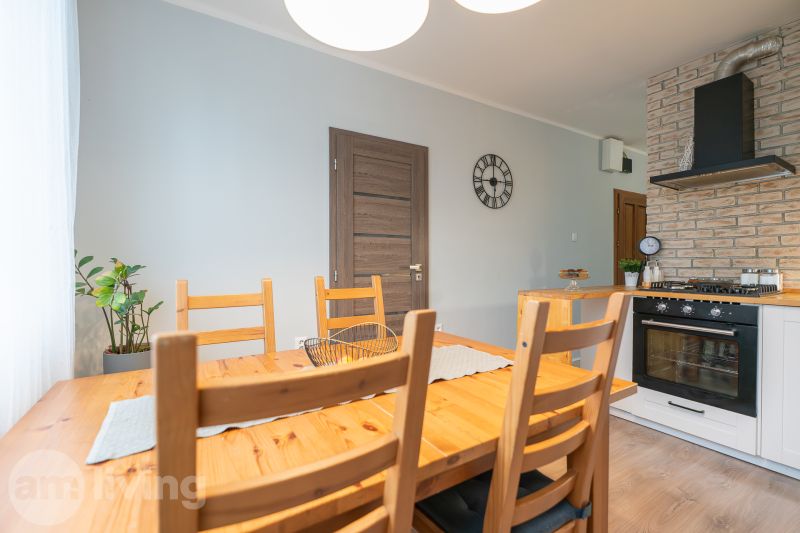 Dining area in a 3-room apartment with a wooden table, brick cladding, and a clock on the wall.