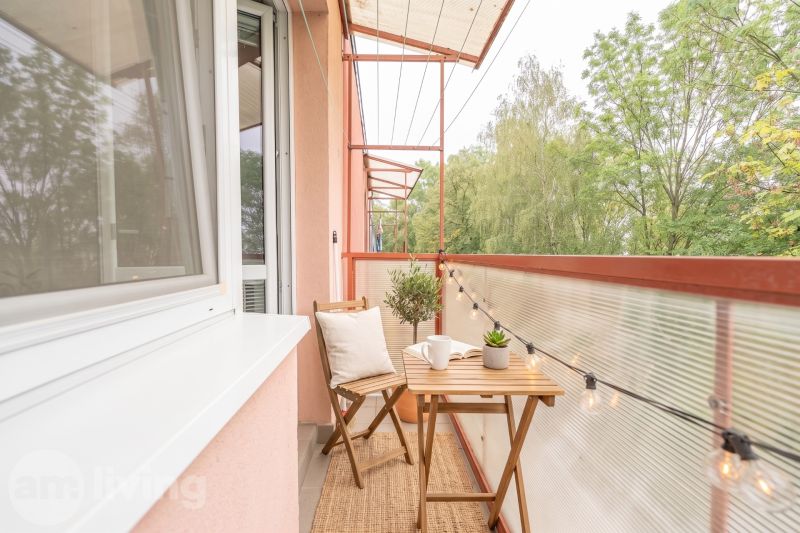 A balcony with wooden furniture and lighting in a 3-room apartment with a view of greenery.