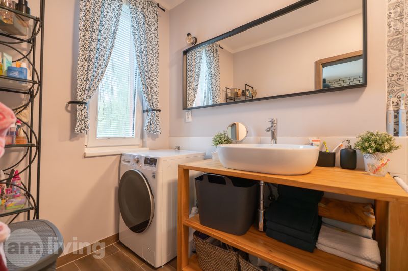 Bathroom in a 3-room apartment with a sink, washing machine, mirror, and window with floral curtains.