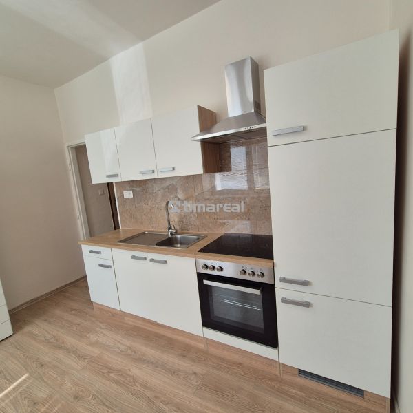 A kitchenette in a studio apartment with white cabinets and a wooden decor floor.