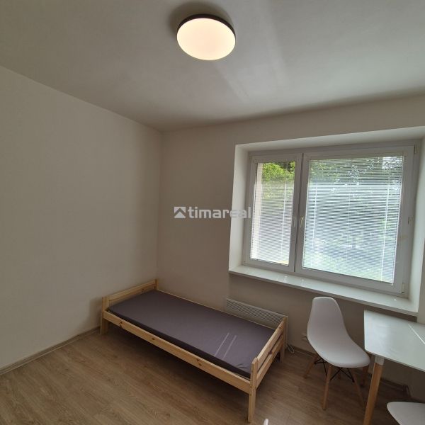 Single bed, table with a white chair, wooden decor flooring, and a window.