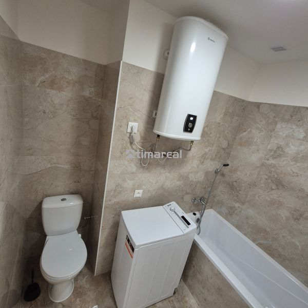 A bathroom in a studio apartment with a bathtub, washing machine, and boiler. The walls are tiled.