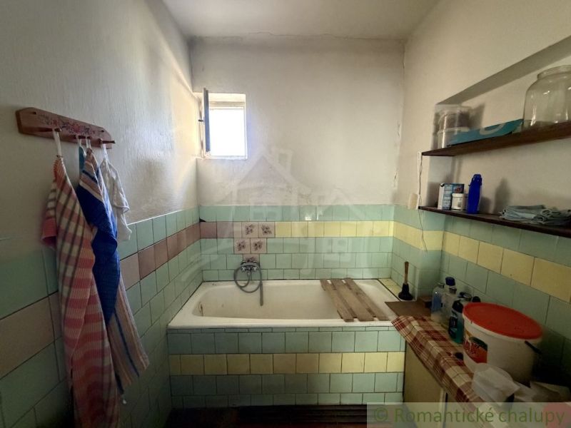 A bathroom in a family house with a bathtub, tiles, and shelves with toiletries.