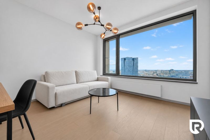 A room with a sofa, a table, a large window, and a wooden-patterned floor in a two-room apartment.