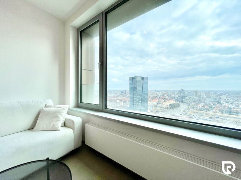 A bright living area of a 2-room apartment with a view of the city skyline through a large window.