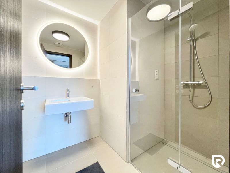 A bathroom in a 2-room apartment with a shower and a round mirror.