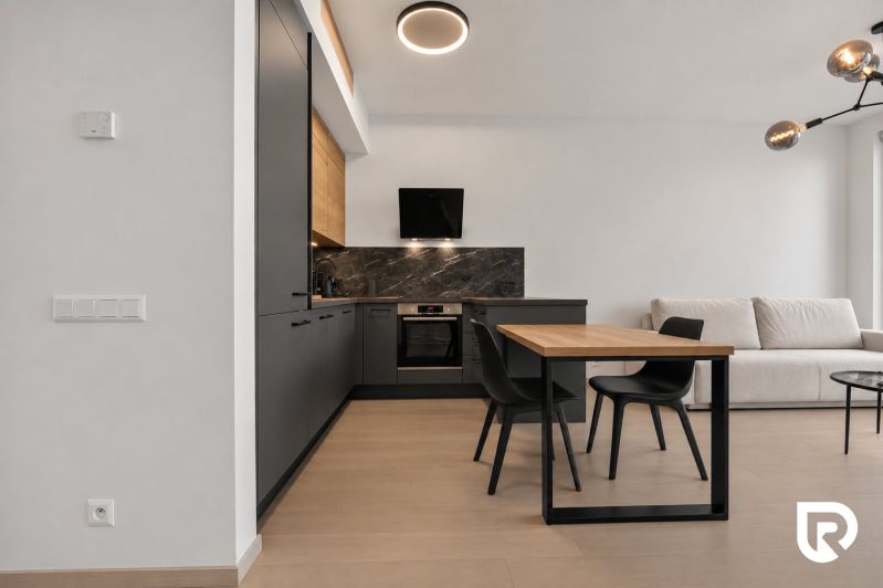 A kitchen with dark cabinets, a sofa, a dining table, and a wooden decor floor in a 2-room apartment.