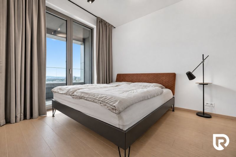 Bedroom with a large window, bed, and lamp in a 2-room apartment.