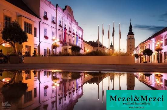 Historical buildings in Trnava are reflected in the water at dusk.