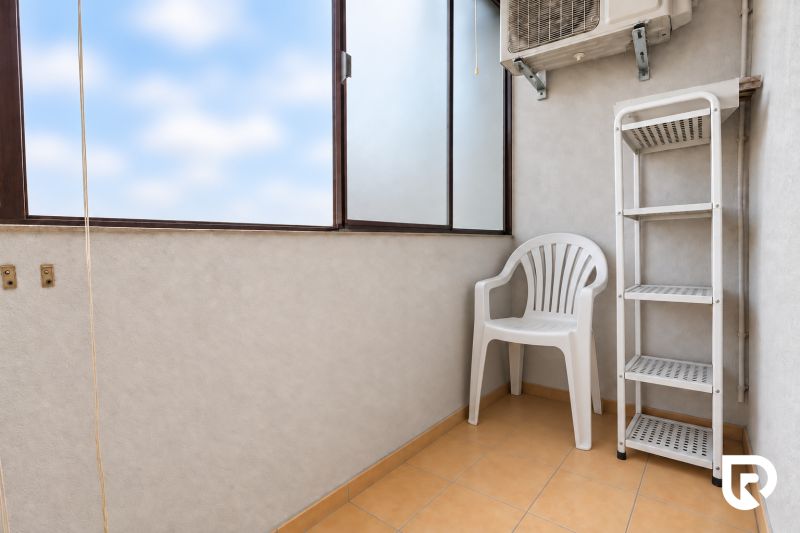 A balcony in a 3-room apartment with a plastic chair, a shelf, and air conditioning.