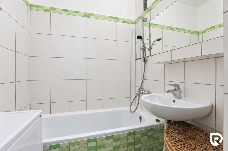 A bathroom with a bathtub, a sink, and green tiles in a 3-room apartment.