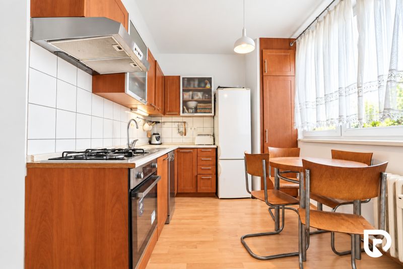 A kitchen in a 3-room apartment with a wooden decor floor, a kitchenette, and a dining table.
