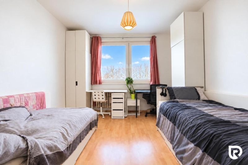 A bright room with two beds, a desk, and a floor with a wooden decor.