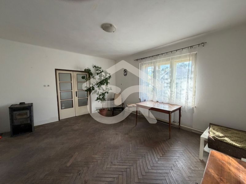 A room in a family house with a large window, a table, and a floor with a wooden decor.