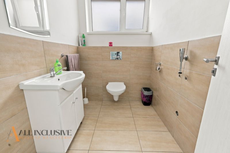 White bathroom in offices with a sink, mirror, and toilet, floor with wooden decor.