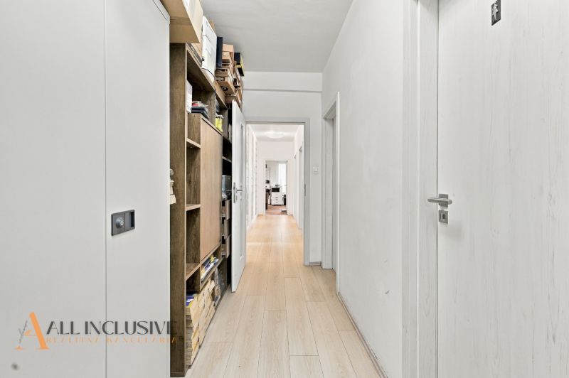 A white corridor with wooden decor, shelves, and doors leading to offices.
