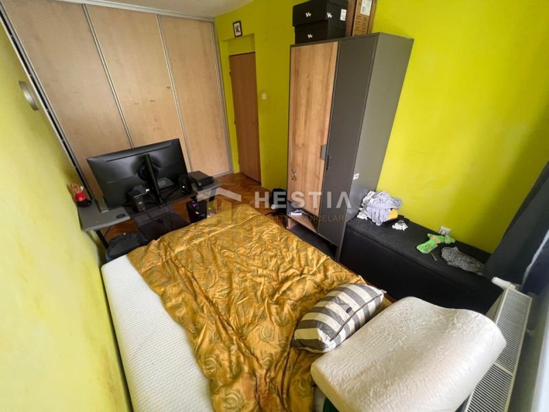 A bedroom with yellow walls, a bed, a table, and cabinets in a three-room apartment.
