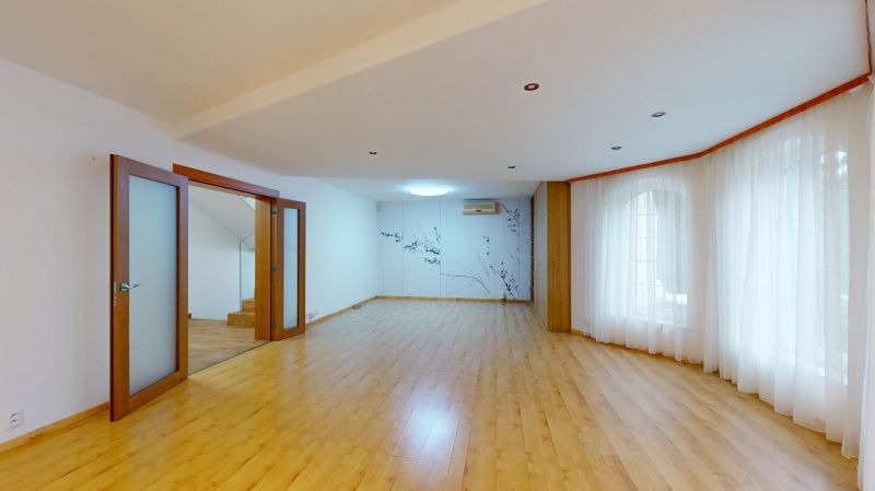 Spacious living room with light curtains and wood-patterned flooring.