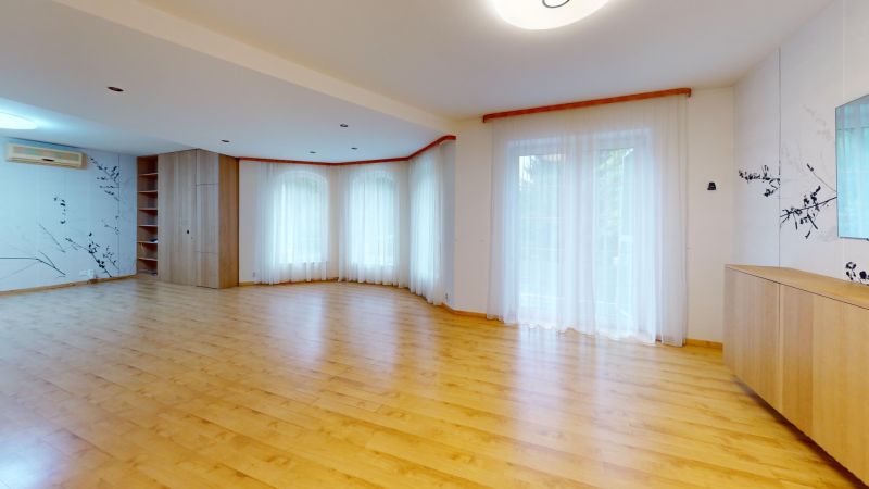 A spacious living room with a wood-patterned floor and light curtains in a family house.