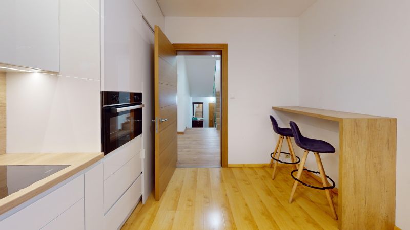 A kitchen in a family house with a wooden decor floor and bar seating.
