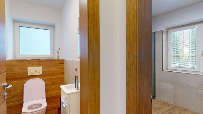 A toilet with a wooden decor wall, a sink, and a window in a family house.