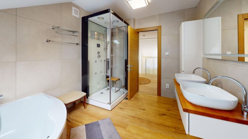 A bathroom in a family house with two sinks, a shower corner, and a floor with a wooden decor.