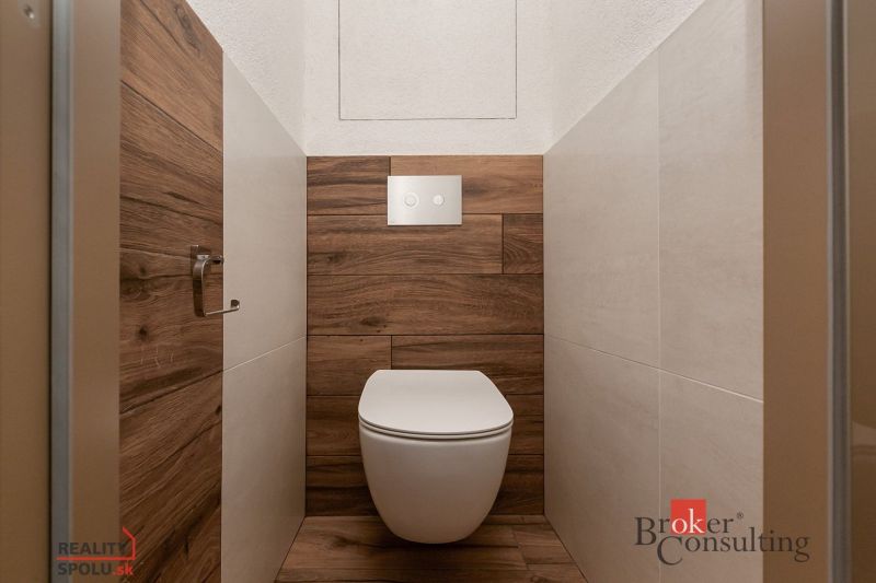 A toilet with a wooden decor and concealed flushing in a 5 or more room apartment.