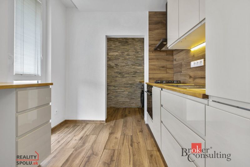 A kitchen with a wooden decor floor, white cabinets, and stone wall cladding.