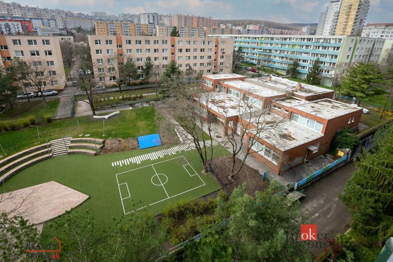 A view of the schoolyard with a playground and residential blocks on Donnerova Street in Karlova Ves.