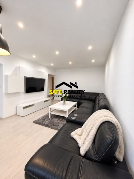 Living room in a 3-room apartment with a large black sofa and a wooden decor floor.