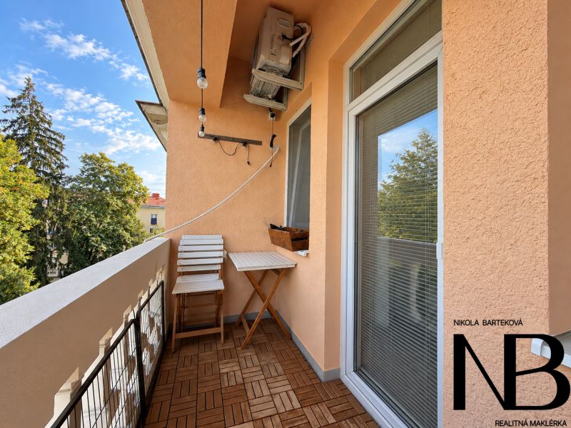 A balcony in a 3-room apartment with wood-patterned flooring and a view of greenery.