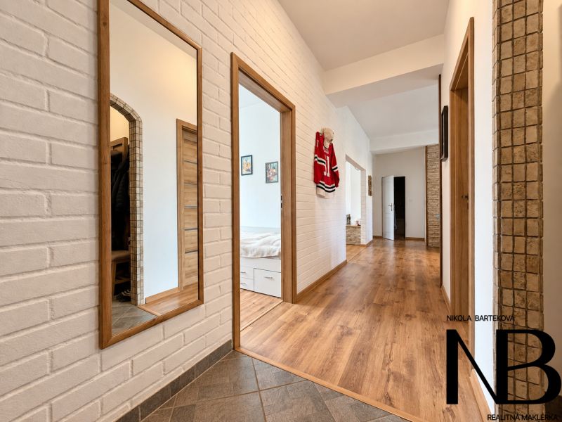 A hallway in a 3-room apartment with a wooden decor floor and mirrors on a brick wall.