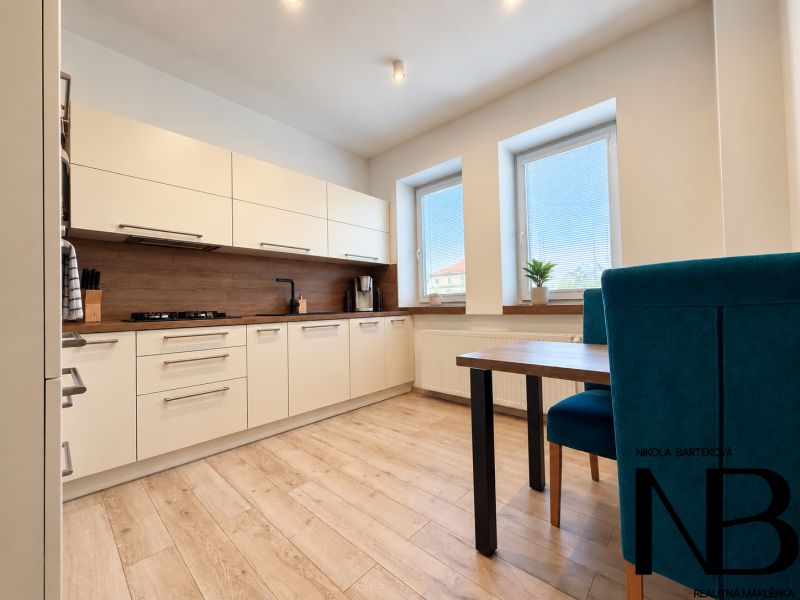 A kitchen with white furniture and a wooden decor floor in a 3-room apartment.