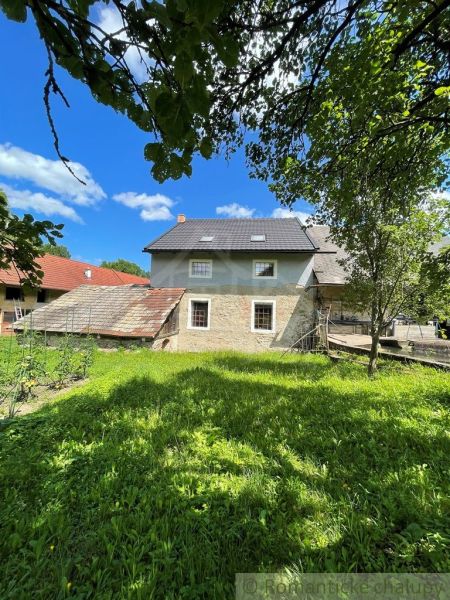 A family house in Mokrá Lúka with a garden, surrounded by trees and a blue sky.
