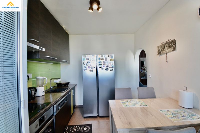A kitchen in a 3-room apartment with white walls, stainless steel appliances, and a dining table.