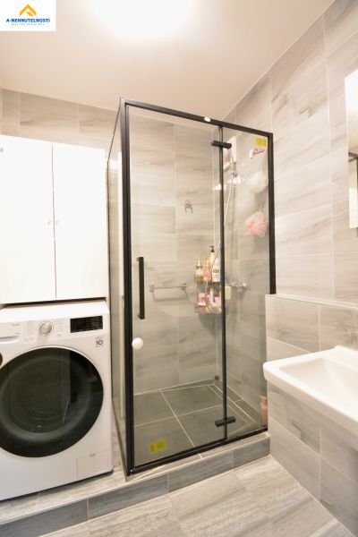 A bathroom with a washing machine, shower, and storage space in a 3-room apartment.