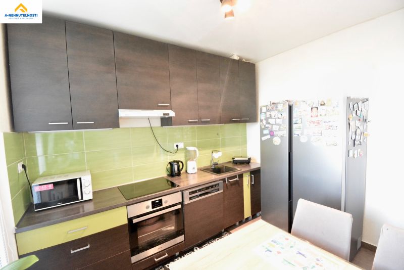A kitchen with dark cabinets, green tiles, and appliances in a three-room apartment.