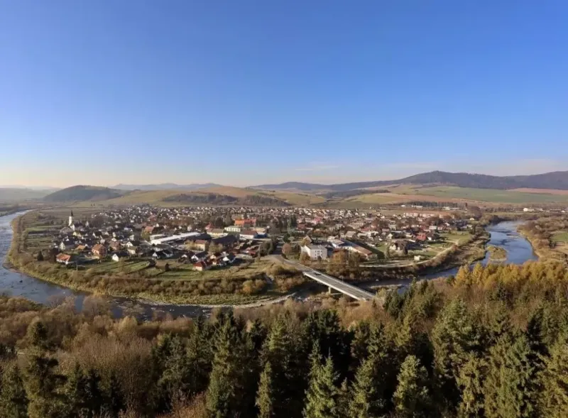 Panorama of agricultural and forest lands in Plavča with a river and a bridge in the background of the forest.