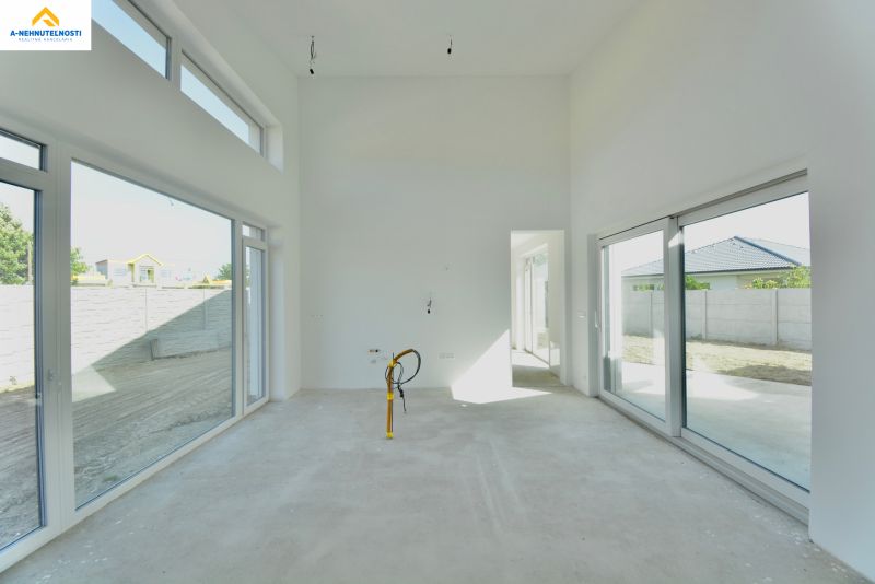 A spacious bright interior of a family house with large windows and an unfinished floor.